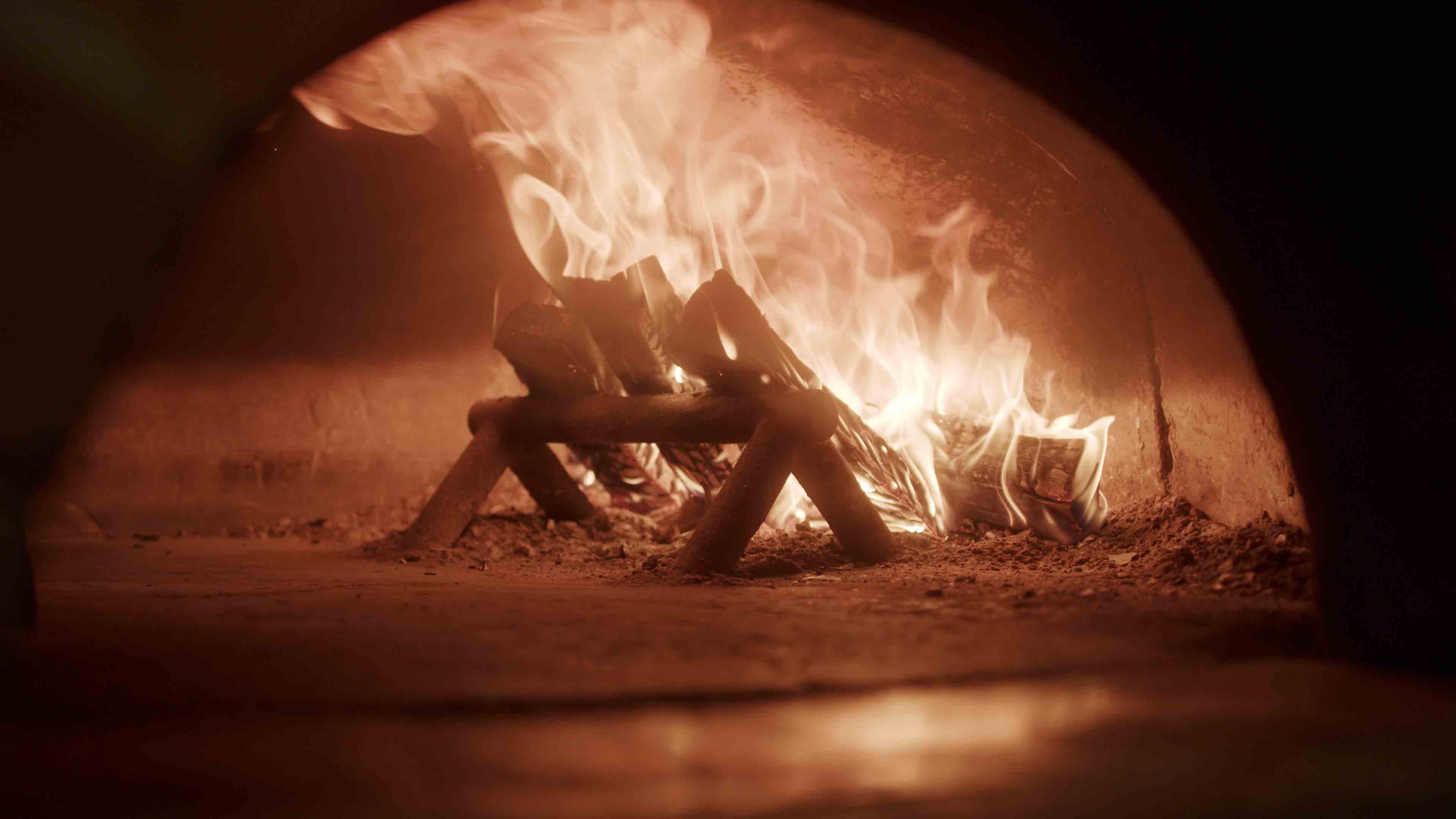 Feuer, das auf Holzscheiten in einem Stein- oder Lehmofen brennt, mit aufsteigendem Rauch.